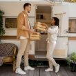 Man and woman handing provisions to one another in front of an RV.