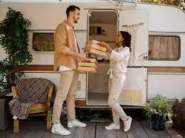 Man and woman handing provisions to one another in front of an RV.