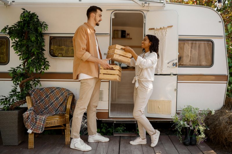 Man and woman handing provisions to one another in front of an RV.