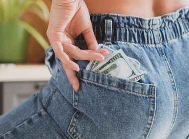 Woman pulling hundred dollar bills out of the back pocket of her jeans.