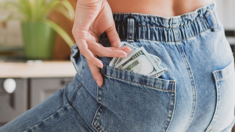 Woman pulling hundred dollar bills out of the back pocket of her jeans.
