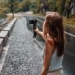 Woman vlogger recording herself next to a wooded mountainside, road, and stream.