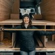 Woman holding a measuring tape while standing in front of an RV in construction in cool weather.