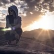 Hooded woman kneeling in the desert looking around as the sun starts to set.