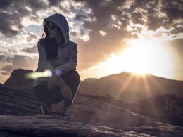 Hooded woman kneeling in the desert looking around as the sun starts to set.