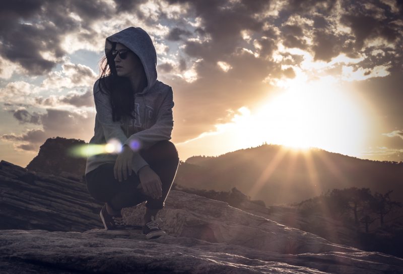 Hooded woman kneeling in the desert looking around as the sun starts to set.