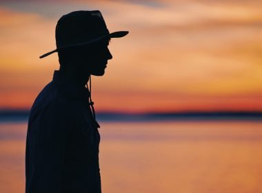 Dark silhouette of a park ranger against a orange and purple sunset sky.