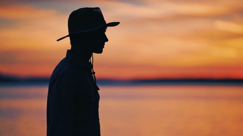 Dark silhouette of a park ranger against a orange and purple sunset sky.