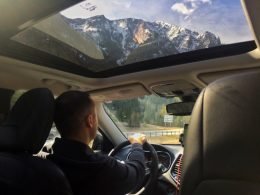 A man drives his tow vehicle through the mountains which can be seen towering above through the sun roof.