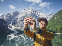 Smiling young traveler using cell phone in the mountains during a hike.