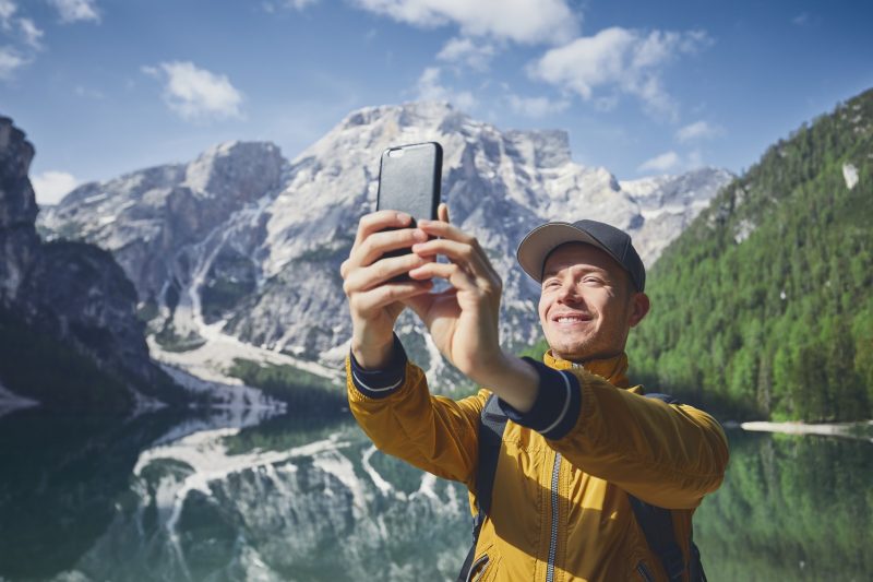 Smiling young traveler using cell phone in the mountains during a hike.