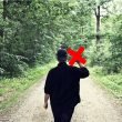 Person walking away from the camera giving the middle finger as they walk down a dirt road in the woods.
