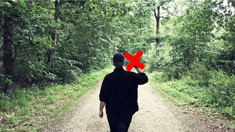 Person walking away from the camera giving the middle finger as they walk down a dirt road in the woods.