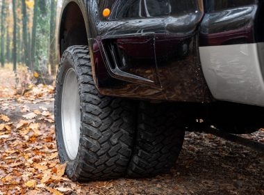 Close up view of the rear tires of a black dually truck parked in the leaves on a fall day.