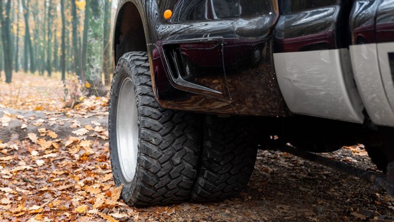 Close up view of the rear tires of a black dually truck parked in the leaves on a fall day.
