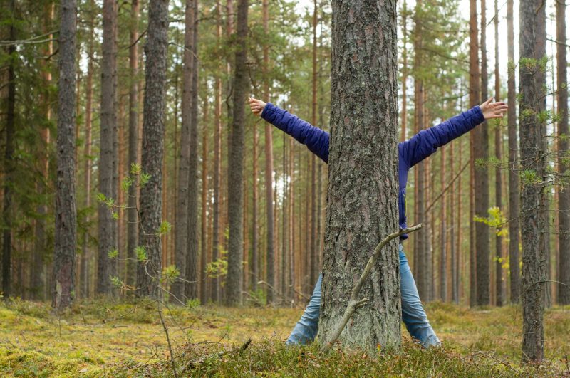 A woman hiding behind a tree with her arms out in exuberance.