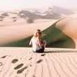 Woman sitting on the top of a sand dune in the desert.
