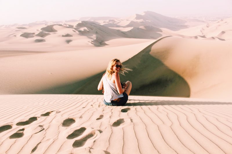 Woman sitting on the top of a sand dune in the desert.