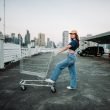 Woman in crop top and jeans pushing a shopping cart in a parking lot.