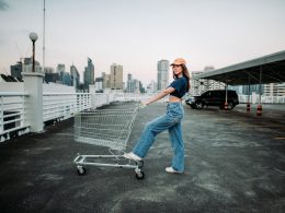 Woman in crop top and jeans pushing a shopping cart in a parking lot.
