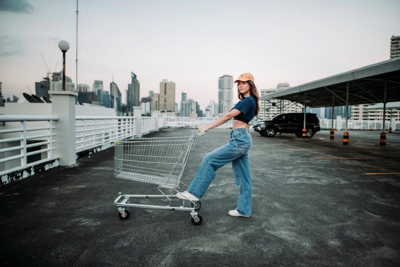 Woman in crop top and jeans pushing a shopping cart in a parking lot.
