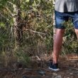 From behind and torso down, a man pees in the woods.