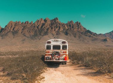 The back of a white skoolie in the desert with rocky mountains in the distance and kids' bikes on mounted on the back.