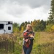 An adult woman wraps a plaid blanket over her shoulders as she walks in contemplation through the woods away fro her travel trailer.