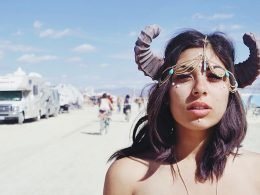 Topless woman wearing horns in the desert where RVs have gathered for a festival.