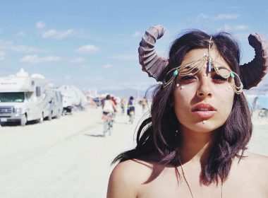 Topless woman wearing horns in the desert where RVs have gathered for a festival.
