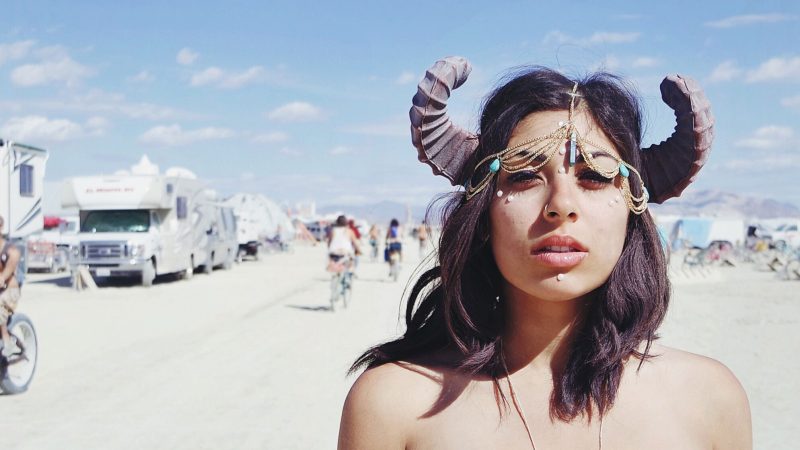 Topless woman wearing horns in the desert where RVs have gathered for a festival.
