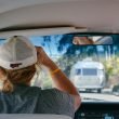 A woman wearing a baseball cap drivers her campervan behind a travel trailer.