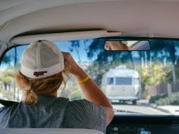 A woman wearing a baseball cap drivers her campervan behind a travel trailer.