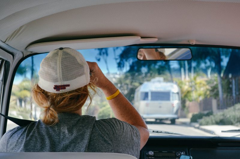 A woman wearing a baseball cap drivers her campervan behind a travel trailer.