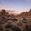A group of friends boondocking out in the desert with an RV, their cars, and a few tents.