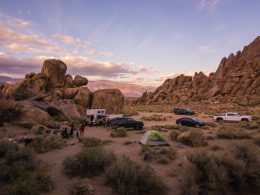 A group of friends boondocking out in the desert with an RV, their cars, and a few tents.
