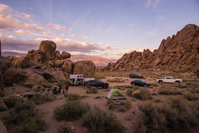 A group of friends boondocking out in the desert with an RV, their cars, and a few tents.