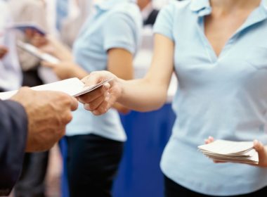A woman hands a brochure to a customer at an RV show