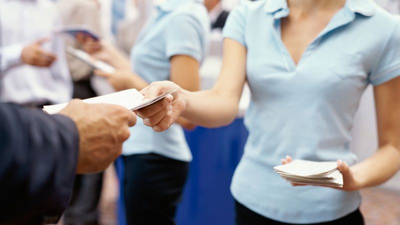 A woman hands a brochure to a customer at an RV show