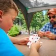 A father and son play a card game at a picnic table while on a camping trip.