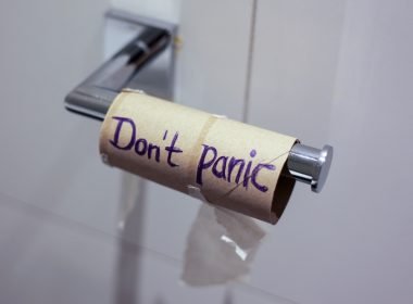An empty toilet paper roll reads "don't panic" on the tp holder in a bathroom.