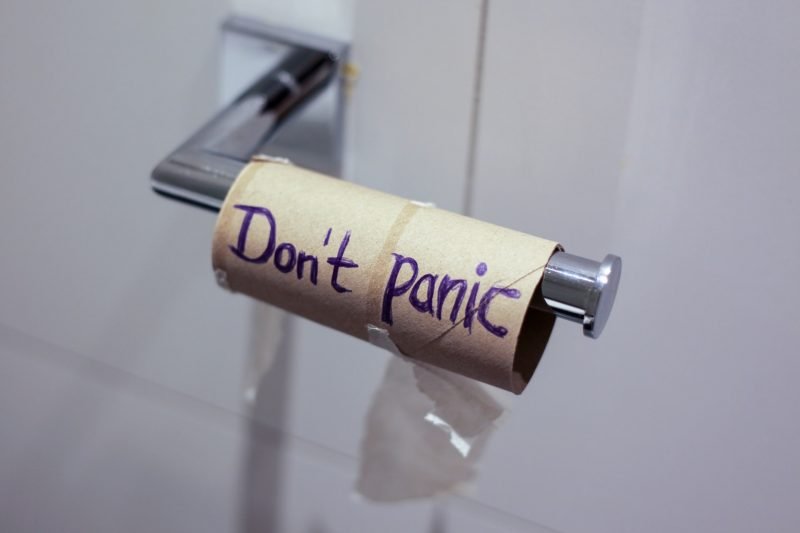 An empty toilet paper roll reads "don't panic" on the tp holder in a bathroom.