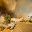 A en emergency vehicle drives out of thick smoked from a wildfire burning on both sides of a road.