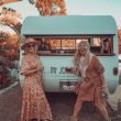 Two women dressed in boho garb outside their vintage mobile with cocktails.