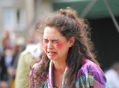 A sad, young woman waering too much makeup sobs outside