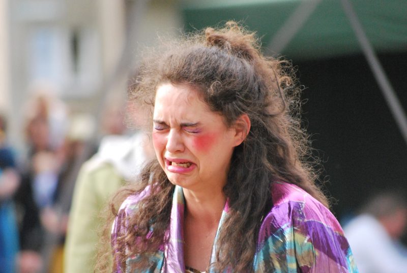 A sad, young woman waering too much makeup sobs outside