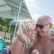 Retired senior couple smiling and laughing, sitting close together poolside.