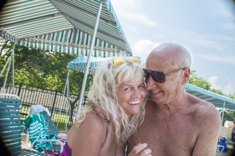 Retired senior couple smiling and laughing, sitting close together poolside.