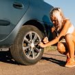 Blonde women in a crop top and shorts changing a tire on a dirt road