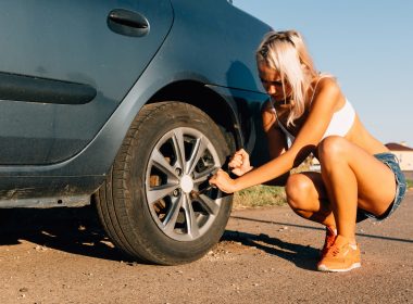 Blonde women in a crop top and shorts changing a tire on a dirt road